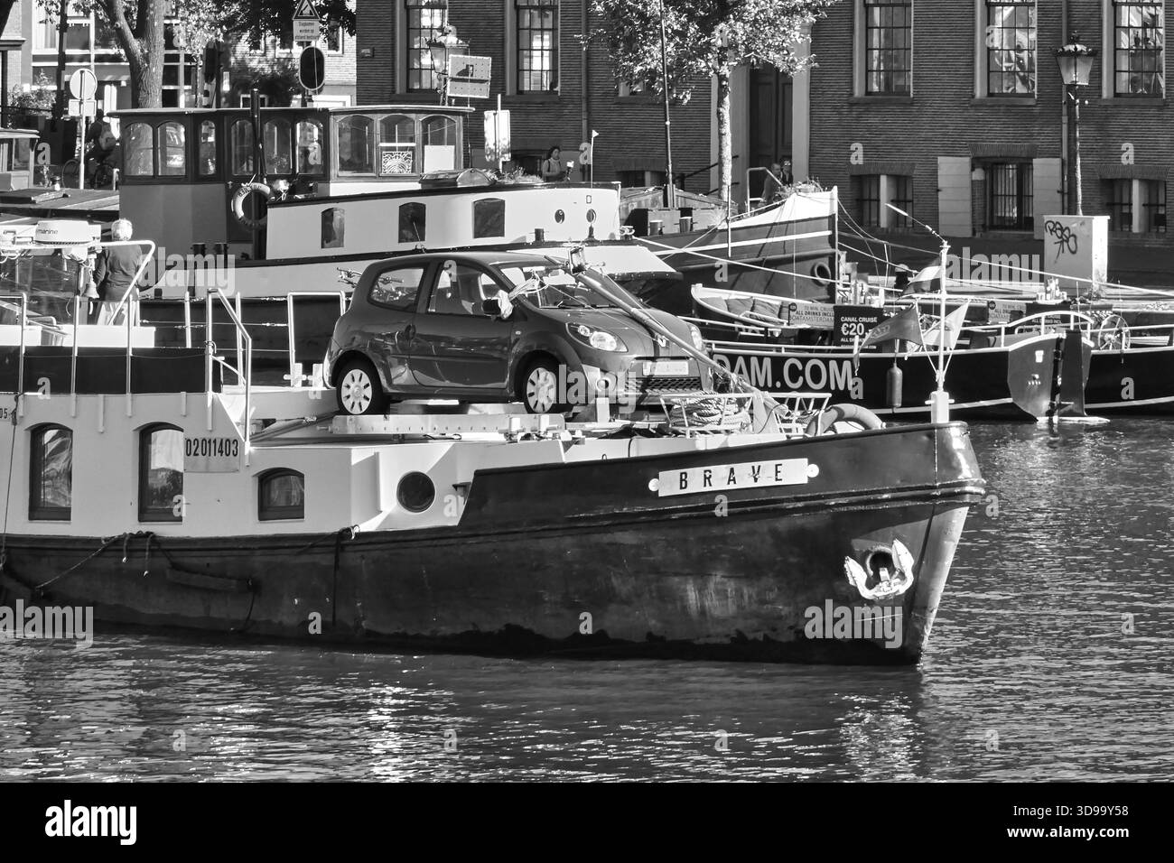 Auto su una chiatta nei canali di Amsterdam: Vivace scena del porto urbano con chiatte e edifici in mattoni Foto Stock