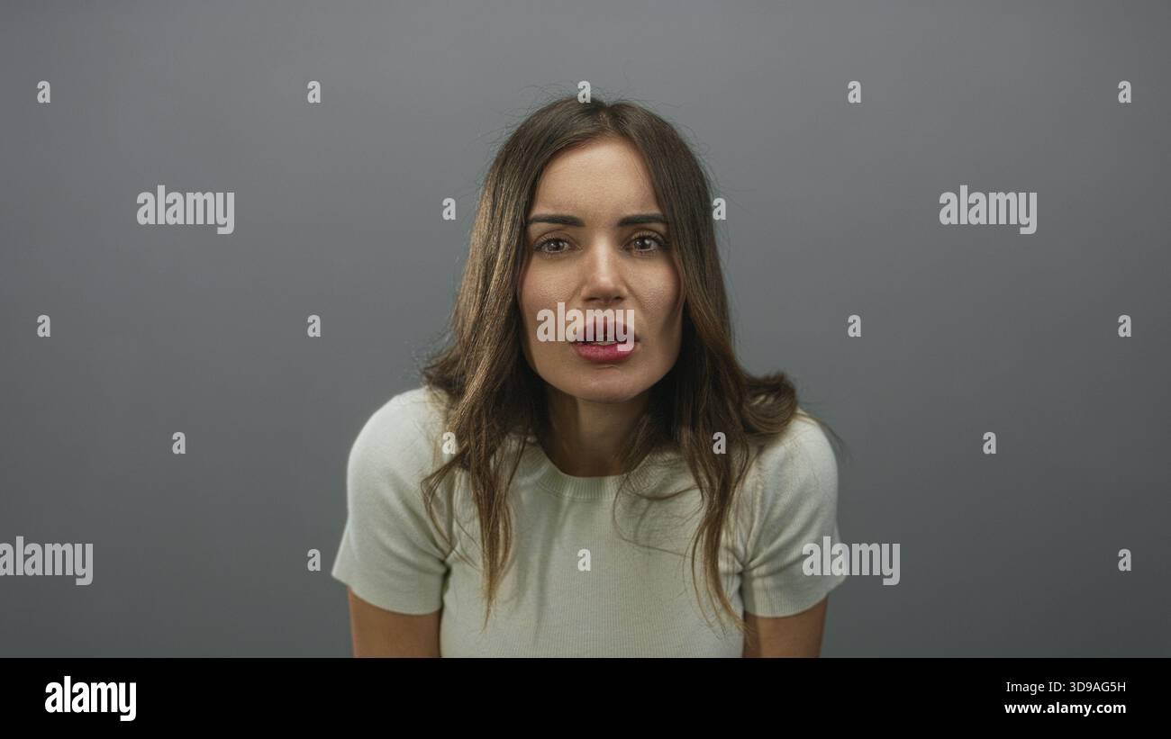 Il volto di una donna guarda la fotocamera in un ambiente da studio minimamente illuminato con sfumature grigie; contemplazione silenziosa. Foto Stock