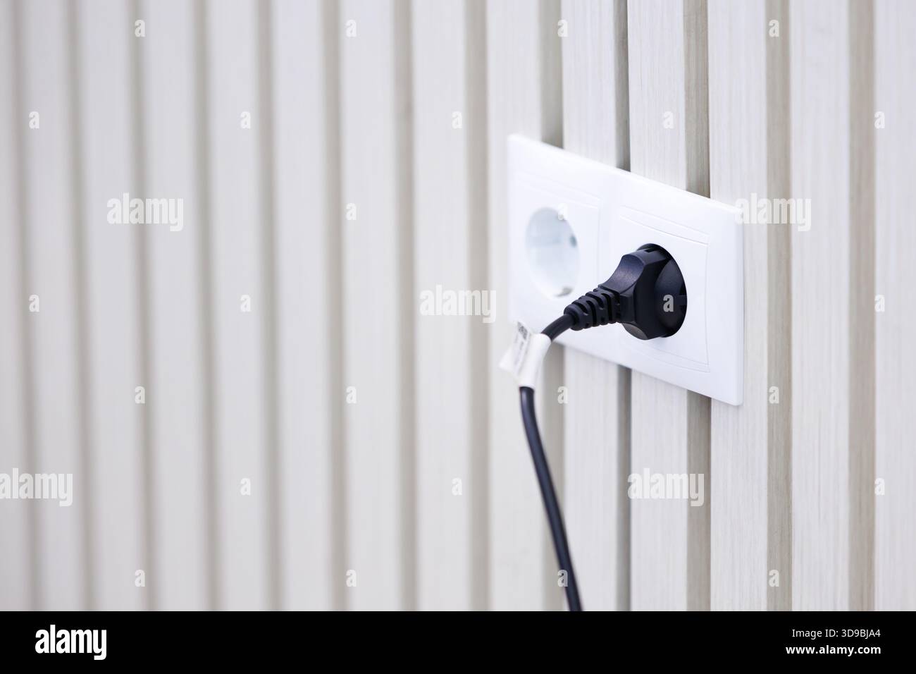 Moderna presa di corrente con cavo collegato su una parete bianca a trama. Scenario minimalista di una presa elettrica con una spina collegata, simbolo di energia, tecnologia Foto Stock