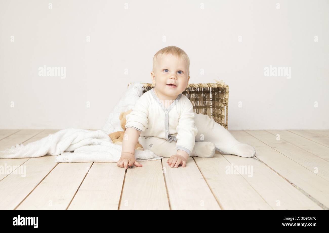 Allegro bimbo in tessuto bianco seduto con coperta e orso sorridente davanti alla fotocamera su sfondo bianco Foto Stock