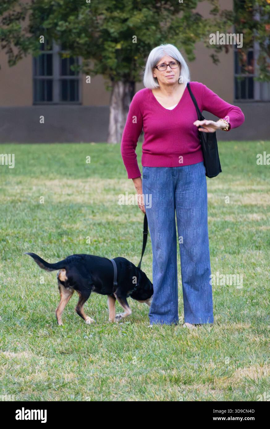 Donna anziana che cammina il suo cane in un parco tranquillo che rappresenta compagnia calma e semplice stile di vita all'aperto. Foto Stock