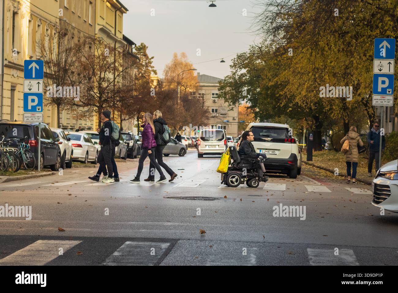 Lubiana, Slovenia 12 novembre 2025 pedoni e utenti di sedie a rotelle attraversano la strada urbana il giorno d'autunno Foto Stock