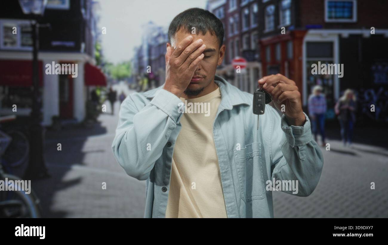 Uomo che tiene in mano le chiavi dell'auto e copre l'occhio con una mano mentre mostra una chiave su una strada trafficata della città, indossa una giacca leggera e una camicia beige; frustrati Foto Stock