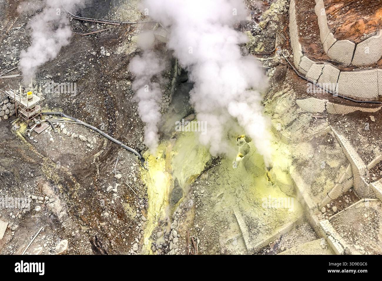 Un campo di fumarole con depositi giallo zolfo e una stazione di monitoraggio del vapore nel cratere di Owakudani, Hakone, Kanagawa, Giappone. Le aree gialle indicano zone in cui lo zolfo elementare si condensa direttamente dai gas che salgono e precipita. A sinistra dell'immagine si trova la stazione di scarico del vapore con la sua struttura metallica Foto Stock