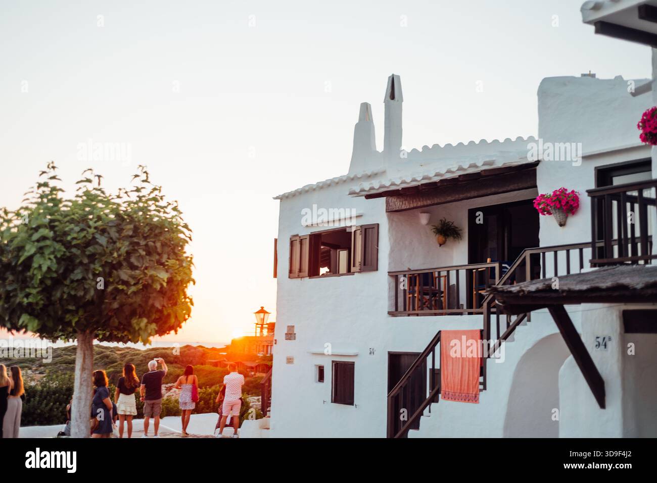 Persone che guardano il tramonto accanto alle case dipinte di bianco a Binibeca, Minorca Foto Stock