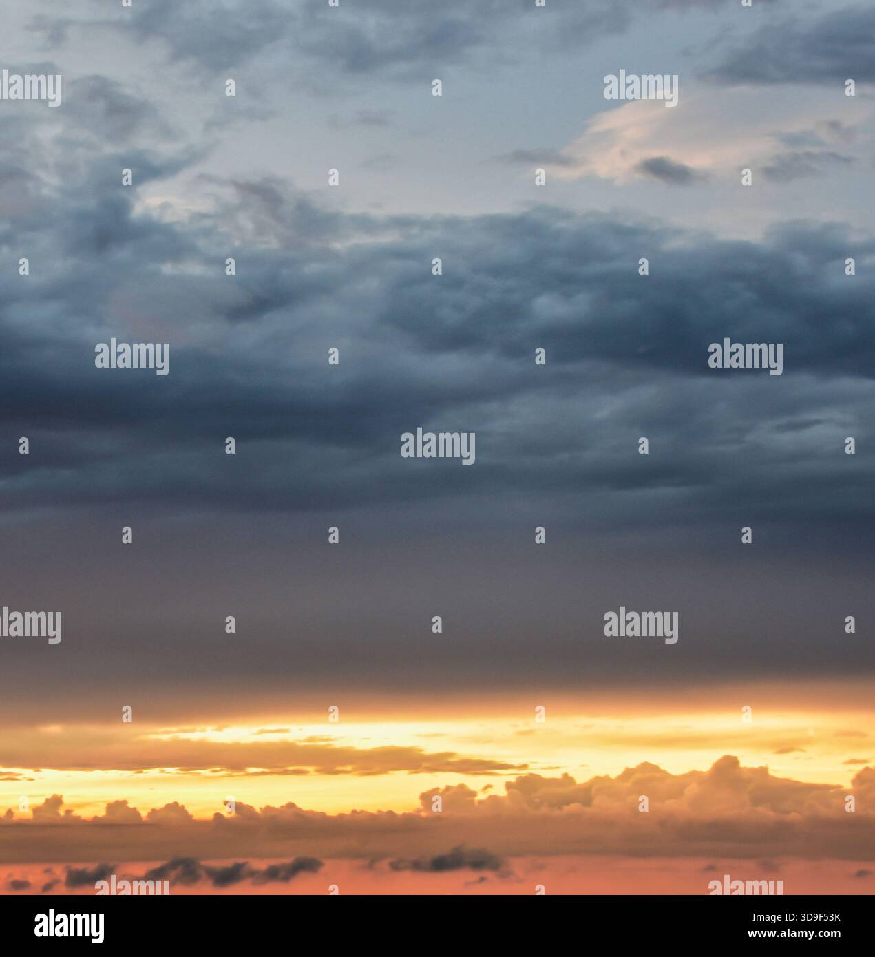 Il cielo del tardo pomeriggio mescola calde e luminose tonalità del tramonto con un'oscurità delicata, dando vita a un tranquillo momento visivo arricchito da nuvole delicatamente illuminate. Foto Stock