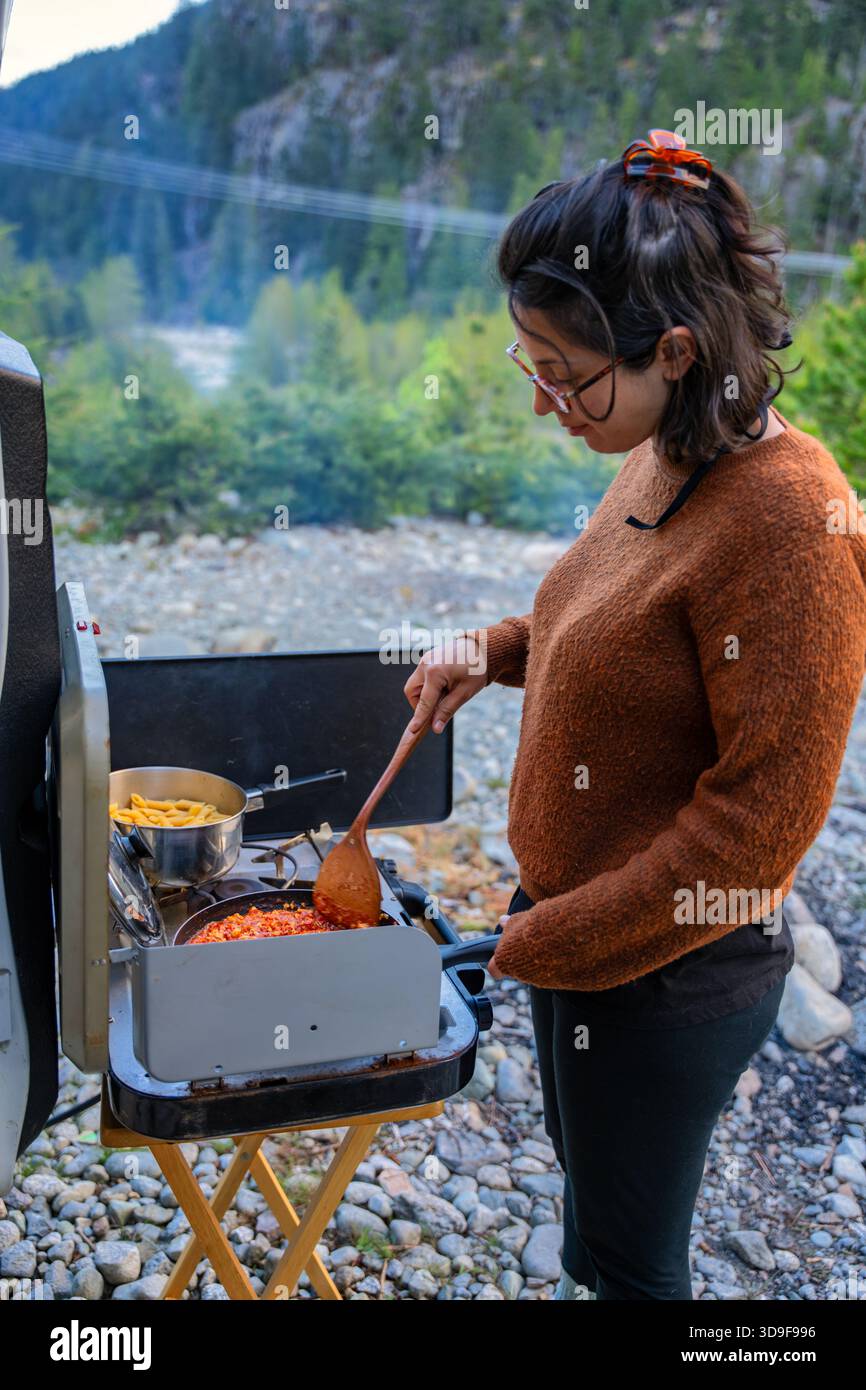 Donna che cucina pasta bolognese fuori camper in montagna Foto Stock