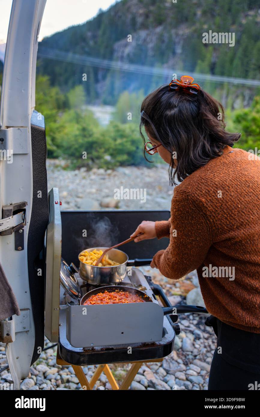 Donna che cucina pasta bolognese fuori camper in montagna Foto Stock