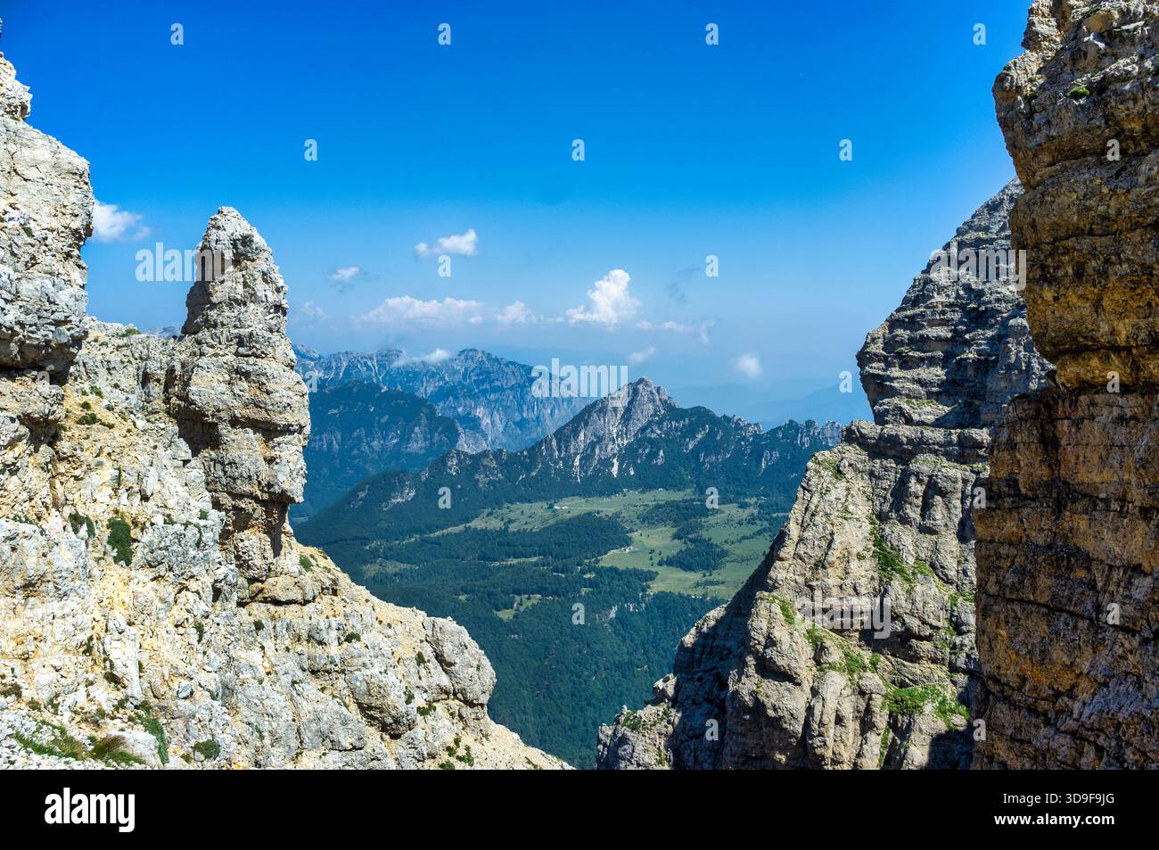 Uno splendido paesaggio montano incorniciato da spettacolari scogliere rocciose, che si affacciano su valli boscose e vette lontane sotto un cielo blu brillante. La scena captu Foto Stock