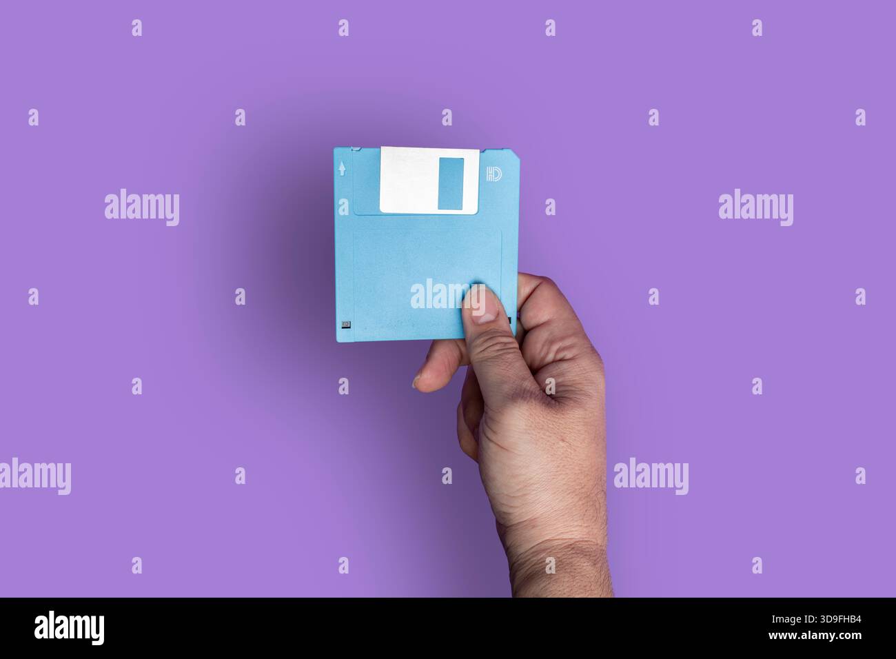 Primo piano della mano di una persona che regge un disco floppy blu su uno sfondo viola, simboleggiando la tecnologia retrò e la memorizzazione dei dati. Foto Stock