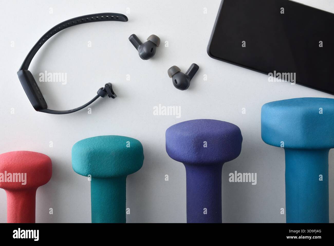 Concetto di sport e tecnologia con vari pesi in neoprene colorati su un piano portapaziente bianco con dispositivi elettronici portatili progettati per lo sport come Foto Stock