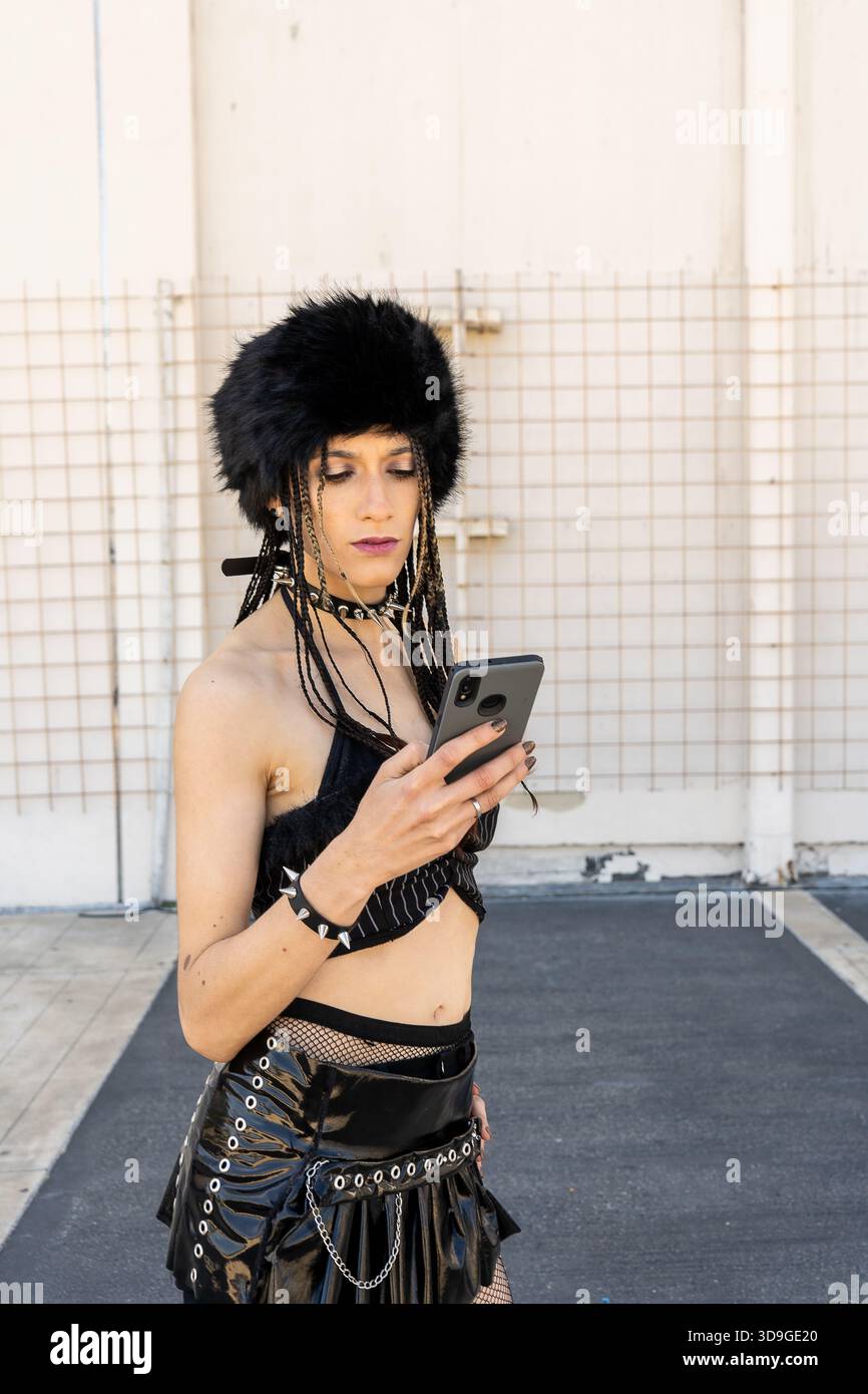 Persona gotica che guarda contenuti su smartphone all'aperto, rappresentando la moda alternativa e la subcultura urbana Foto Stock