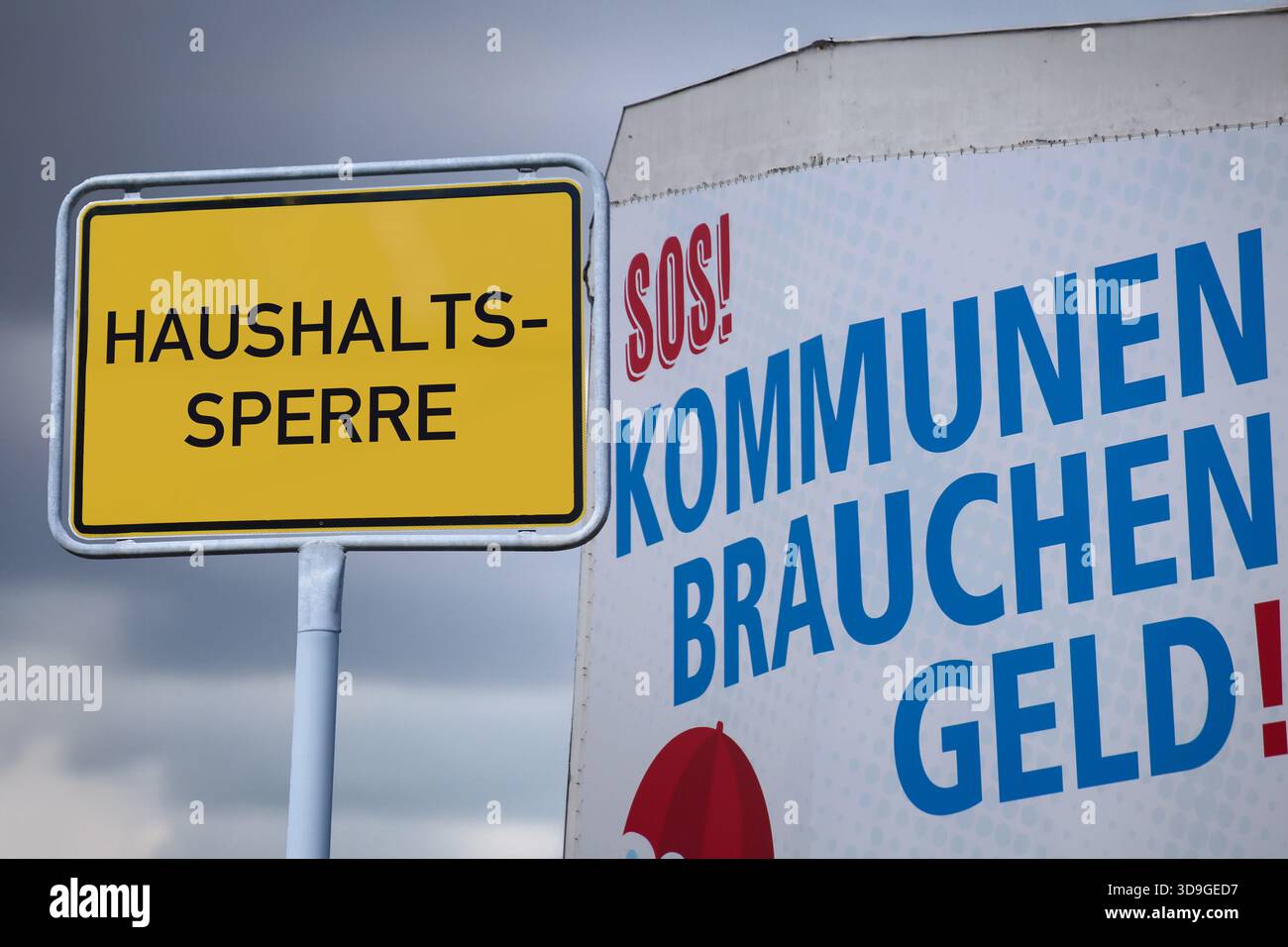 (Montaggio fotografico) cartello d'ingresso della città con la scritta HAUSHALTSSPERRE (congelamento del budget) accanto a un poster con la scritta KOMMUNEN BRAUCHEN GELD (autore locale Foto Stock