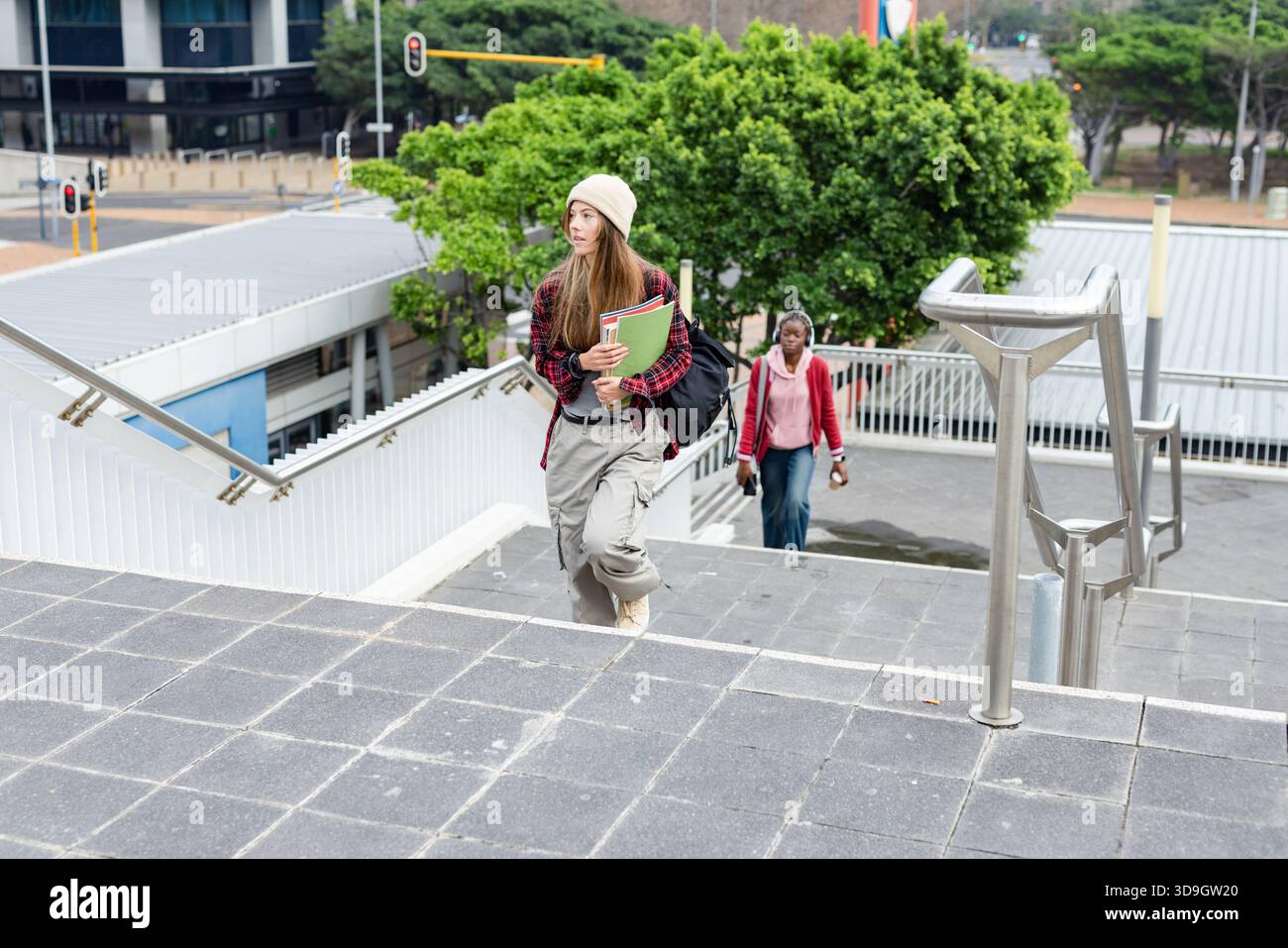 Diverse compagne di classe che salgono gradini in cemento nel campus e trasportano notebook e smartphone con zaino Foto Stock