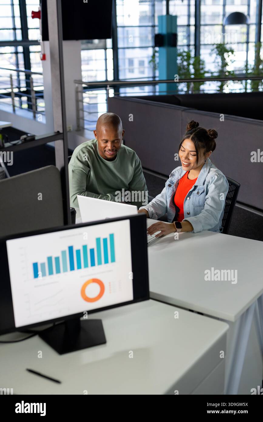 Colleghi diversi che analizzano i grafici a torta e a bar sul monitor mentre lavorano su un notebook alla scrivania open space Foto Stock