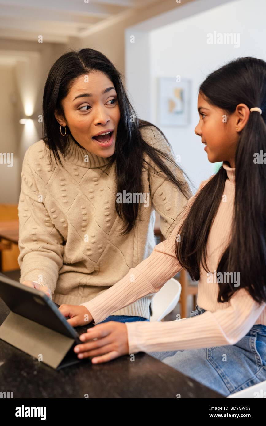 Madre e figlia diverse che si piegano in avanti a sorpresa mentre toccano il tablet al piano di lavoro della cucina Foto Stock