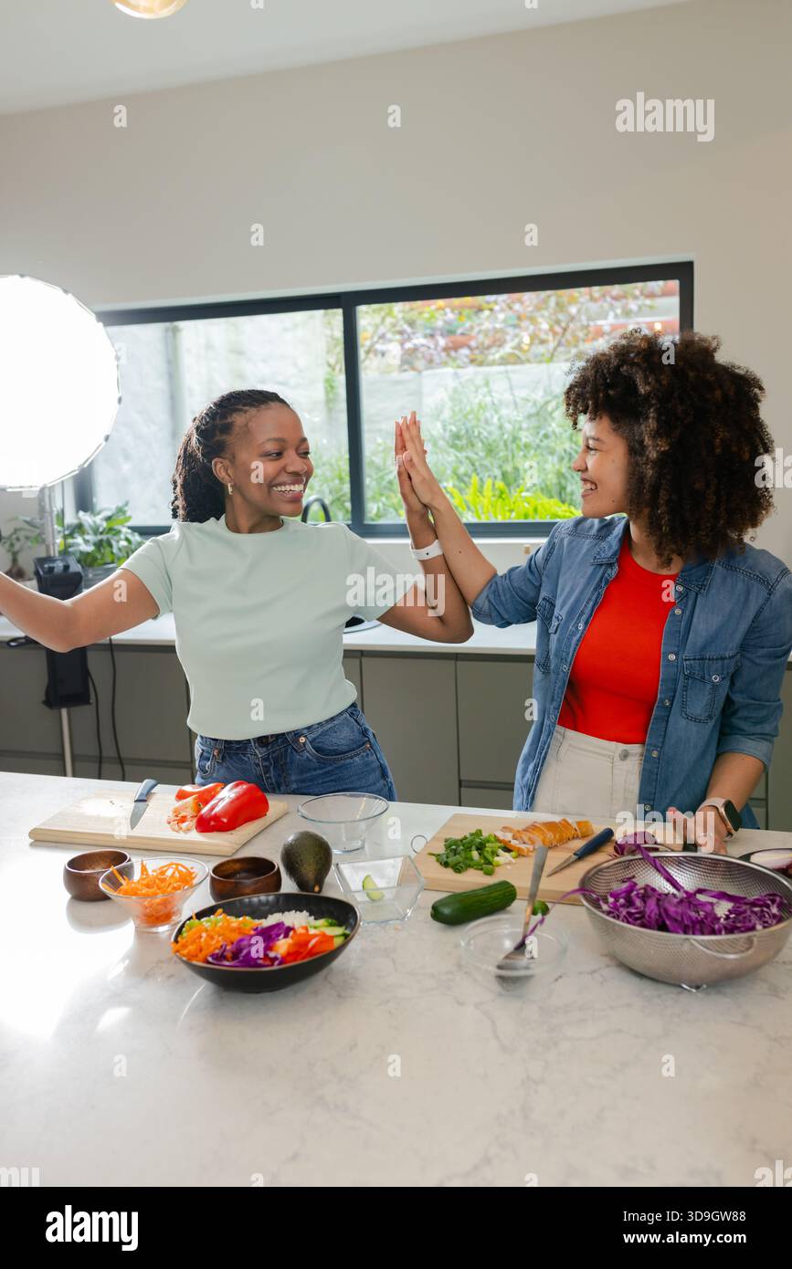 Le donne afro-americane sono amiche di verdure di alta qualità e tagliano su un'isola di marmo con una luce anulare Foto Stock