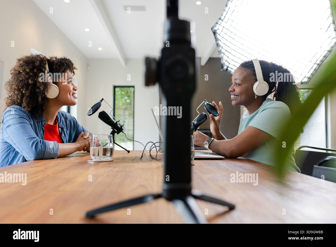 Diverse amiche che registrano podcast in studio utilizzando due microfoni, fotocamera e cuffie Foto Stock