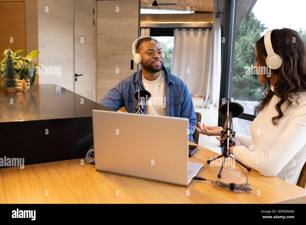 Diversi podcast ospitano lo spettacolo al tavolo di legno in un accogliente studio con computer portatile e microfoni Foto Stock