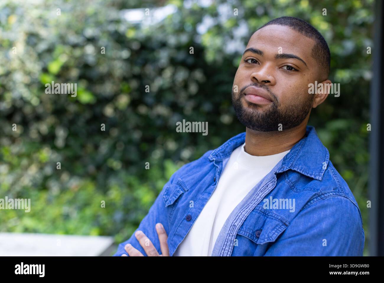 Uomo afroamericano in piedi con le braccia incrociate nel cortile posteriore in camicia bianca, camicia in denim, spazio copia Foto Stock