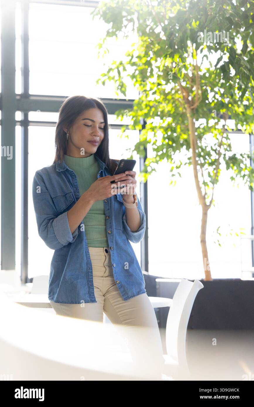 Donna asiatica indiana appoggiata su un tavolo bianco nella sala dell'ufficio utilizzando lo smartphone, spazio fotocopie Foto Stock