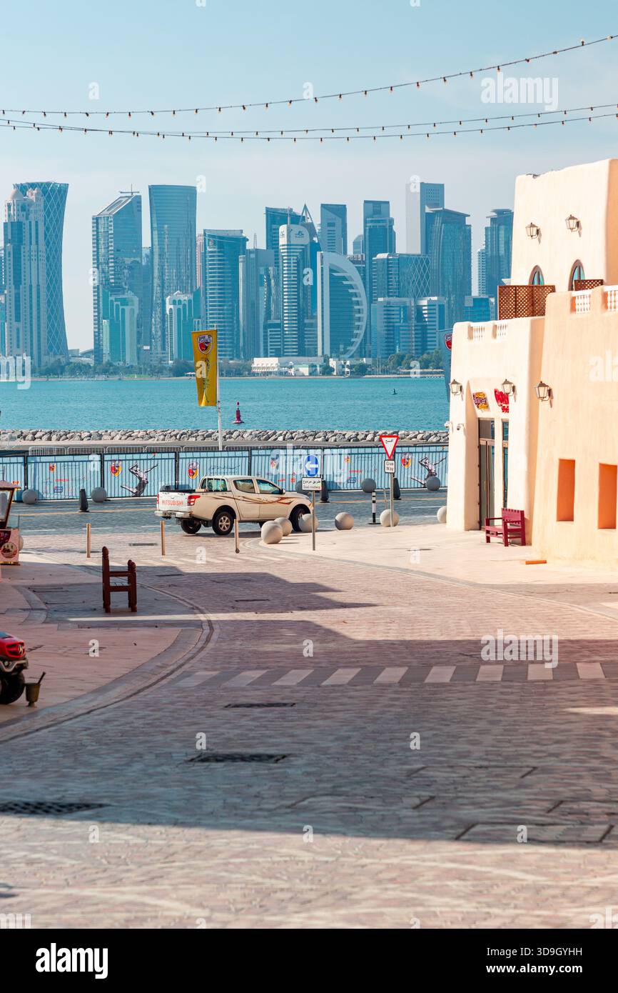 Distretto di mina presso il vecchio porto di Doha in Qatar: 15 marzo 2025. Una passeggiata sul lungomare illuminata dal sole incornicia uno skyline moderno della città oltre le acque calme. Beige stuc Foto Stock