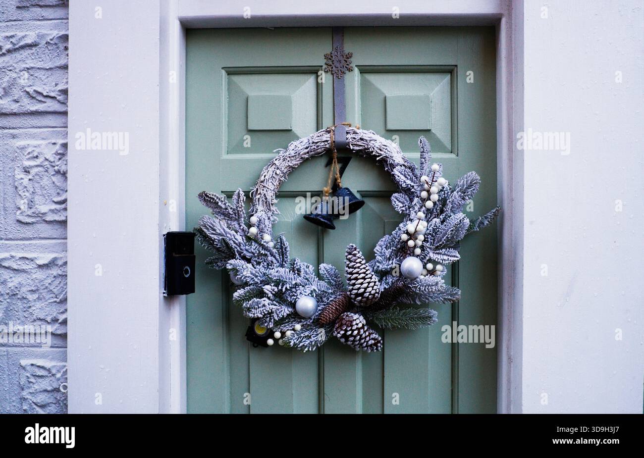 Una corona natalizia su una porta verde salvia con telecamera campanello Foto Stock