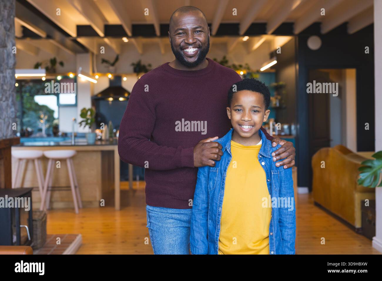 Padre e figlio afroamericani che condividono i sorrisi nella cucina casalinga con l'isola di legno e le piante in vaso Foto Stock