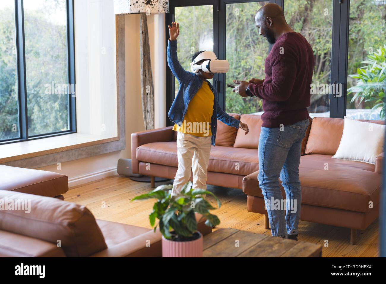 Padre e figlio afroamericani esplorano la realtà virtuale con visore e controller in salotto Foto Stock