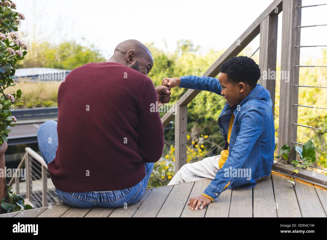 Padre e figlio afroamericani che si scambiano il pugno sul portico vicino alla ringhiera dei cavi con piante in vaso Foto Stock
