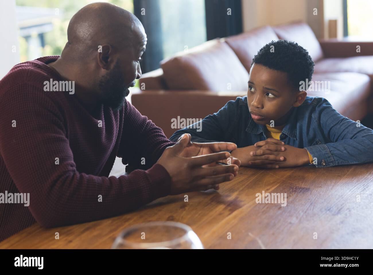 Padre e figlio afroamericani seduti a un tavolo di legno in soggiorno, che gestiscono verso la ciotola di vetro Foto Stock
