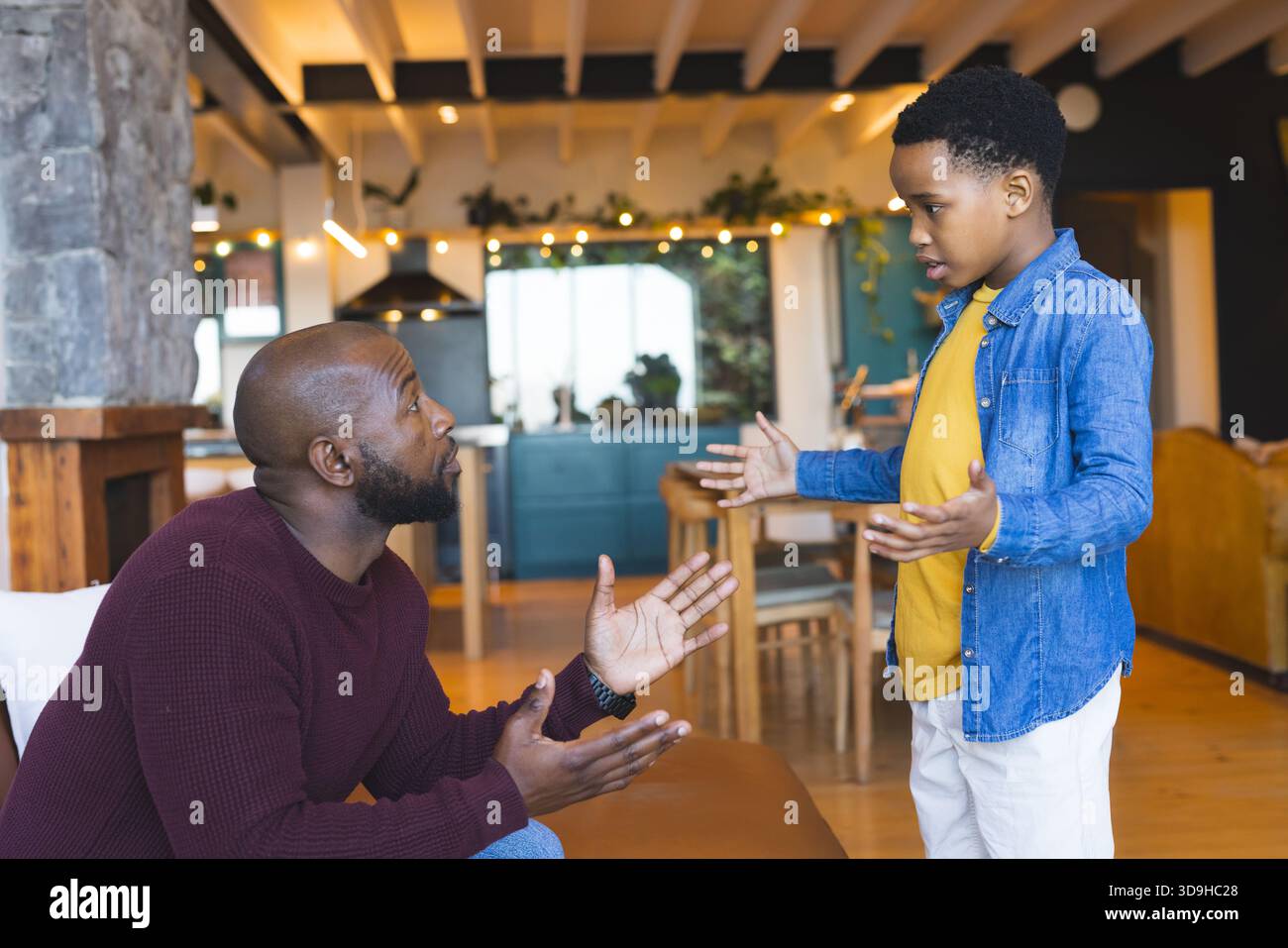 Padre e figlio afroamericani che gestiscono l'uno verso l'altro sul divano in pelle all'interno del soggiorno di casa Foto Stock