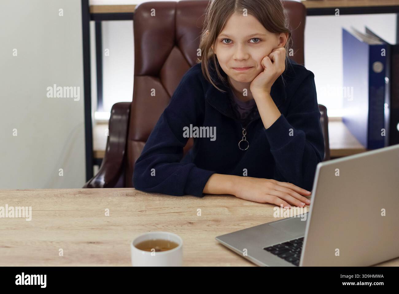 Si è disimpegnato con un maglione blu scuro alla scrivania con un laptop e una tazza in ufficio Foto Stock