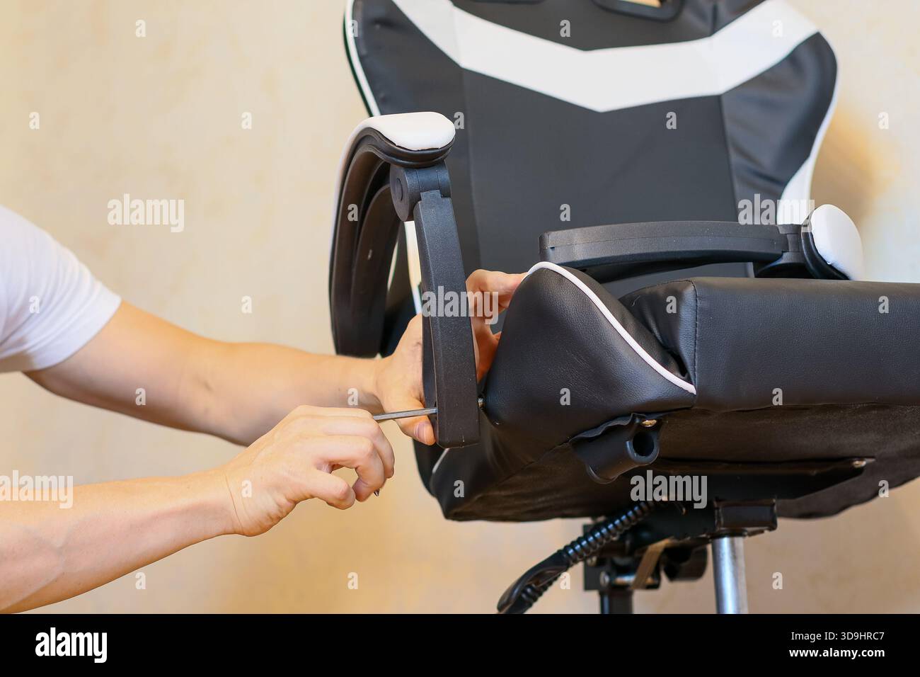 Primo piano della mano di un uomo utilizzando un cacciavite per serrare una vite sul bracciolo nero di una sedia da gioco durante il montaggio. Foto Stock