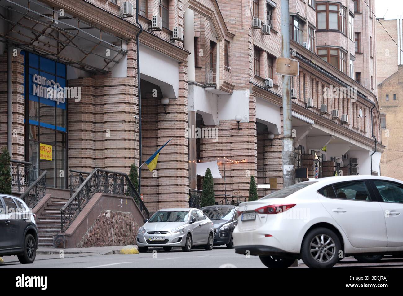 L'architettura in mattoni si erge alta mentre le auto fiancheggiano la trafficata strada della città, catturando la vita quotidiana. Kiev, Ucraina. 5 dicembre 2025. Foto Stock