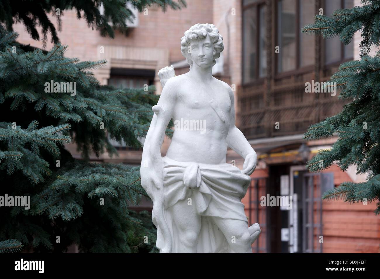 La statua di marmo si erge graziosamente tra pini in un incantevole cortile. Kiev, Ucraina. 5 dicembre 2025. Foto Stock