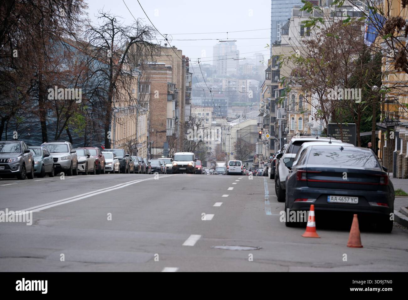 Una strada tranquilla in città con auto parcheggiate e un debole paesaggio urbano sullo sfondo. Kiev, Ucraina. 5 dicembre 2025. Foto Stock