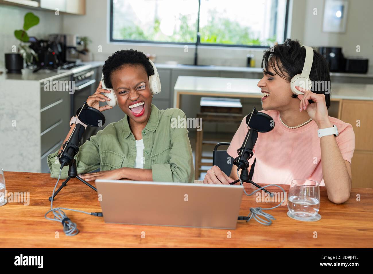 Diversi colleghi seduti al tavolo in cucina registrano podcast con microfoni e computer portatile Foto Stock