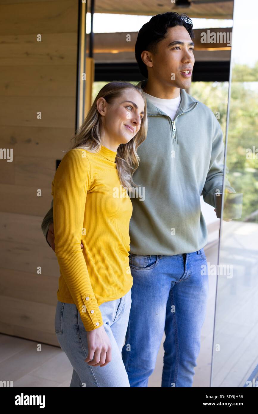 Coppie diverse in piedi e guardando verso l'esterno attraverso la porta scorrevole in vetro di casa con pavimenti in legno Foto Stock
