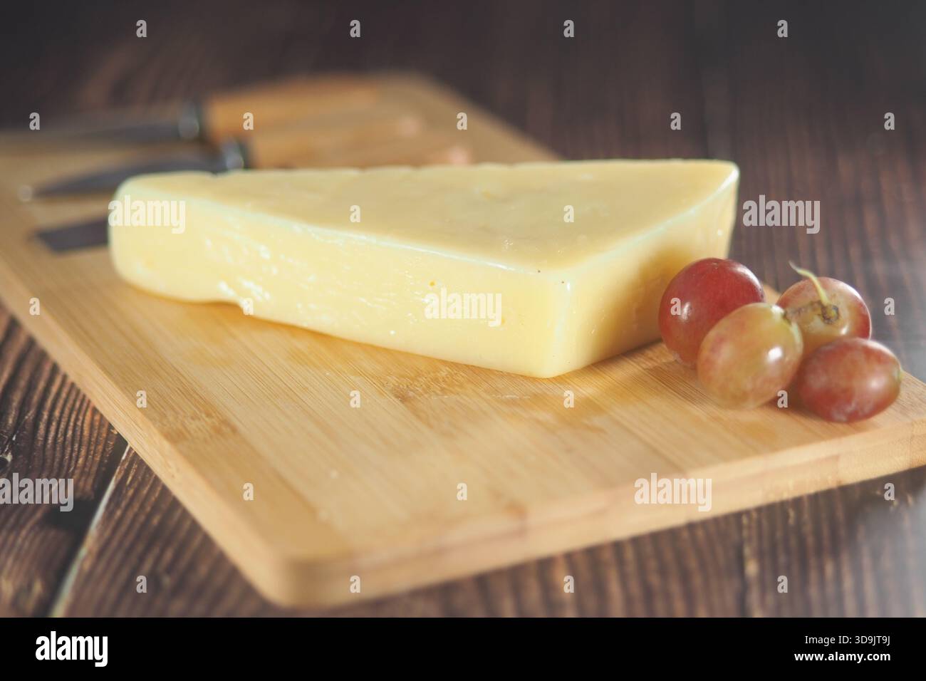 Blocco di formaggio e uva su un tagliere di legno Foto Stock