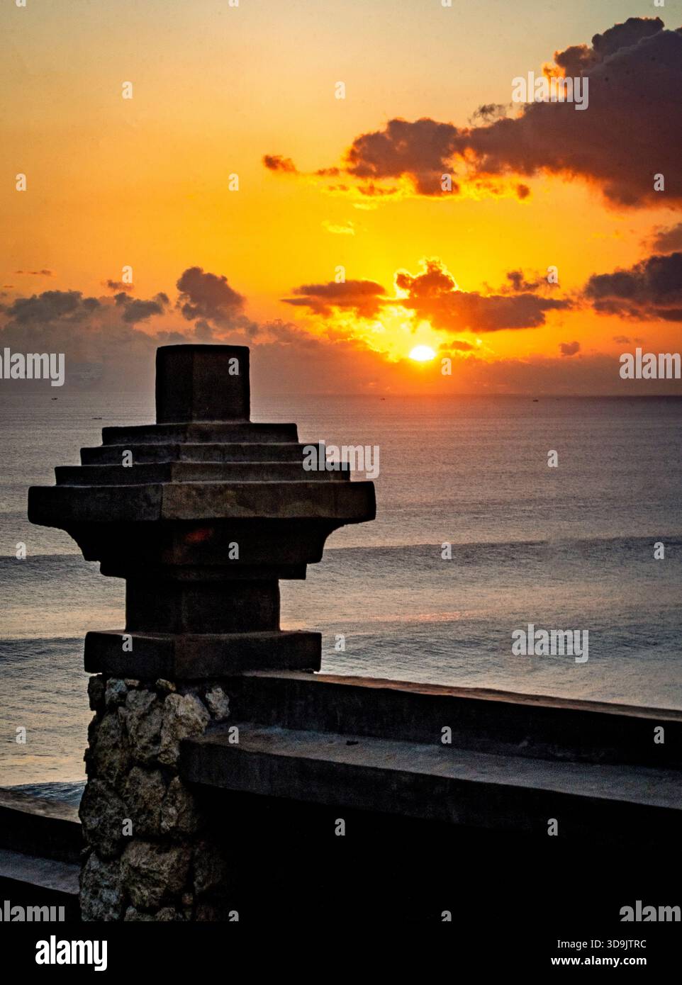Silhouette di una struttura in pietra contro un vibrante tramonto sull'oceano. Foto Stock