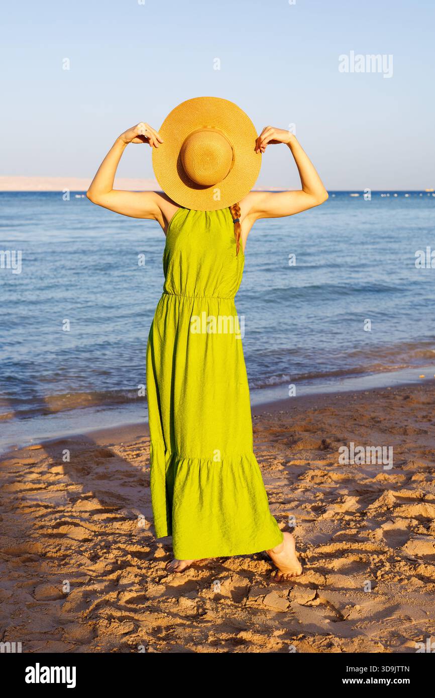 Donna che tiene il cappello di paglia sul viso sulla spiaggia sabbiosa. Foto Stock
