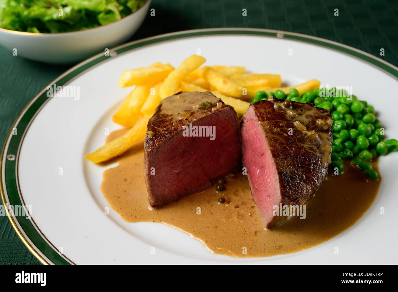Bistecca di manzo con filetto Mignon con salsa peperoncino verde con patatine fritte e piselli chiamata Steak au Poivre Vert in francese Foto Stock