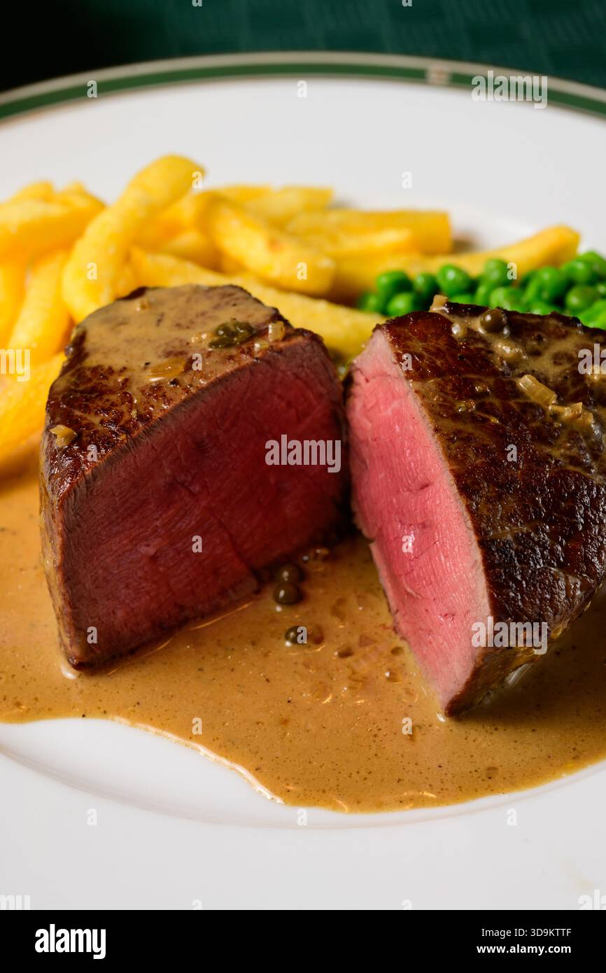 Bistecca di manzo con filetto Mignon con salsa peperoncino verde con patatine fritte e piselli chiamata Steak au Poivre Vert in francese Foto Stock