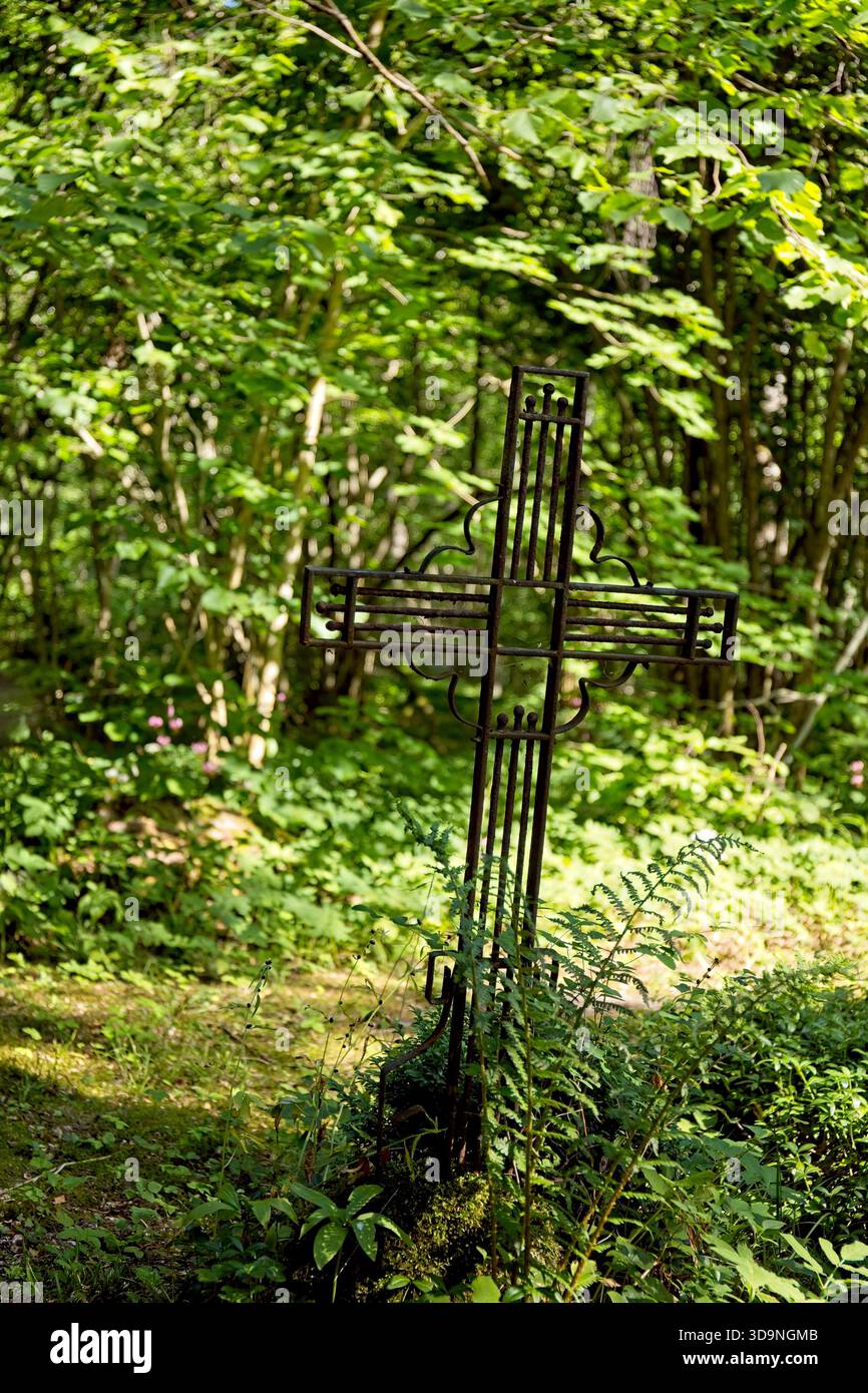 Ornata croce in metallo antico, in un cimitero circondato da vegetazione lussureggiante, cimitero abruzzese, Saaremaa, Estonia. Foto Stock