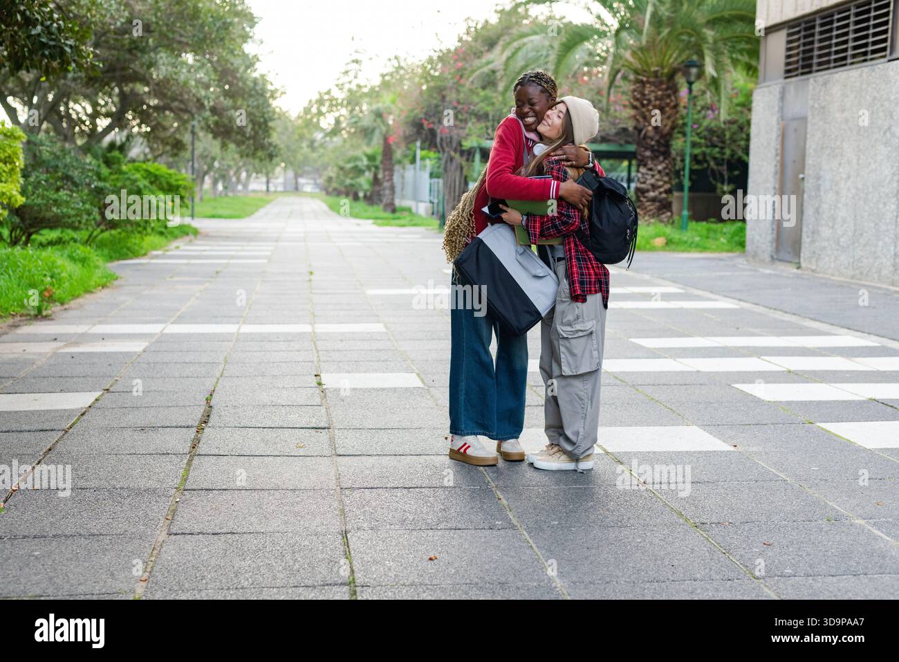 Diverse amiche che abbracciano il vialetto urbano del campus, trasportano borsa tote e zaini, spazio fotocopie Foto Stock