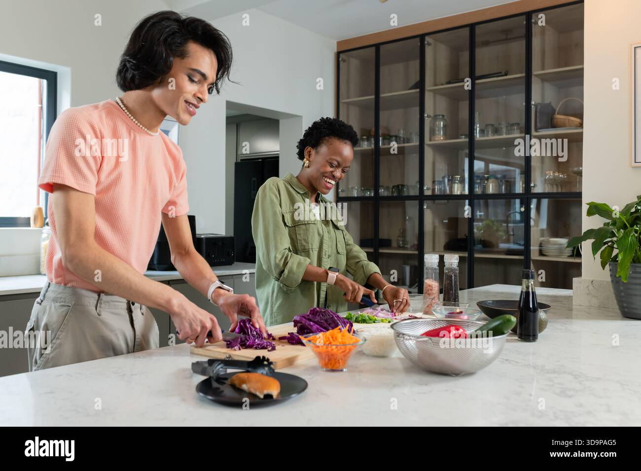 Amici diversi che tagliano verdure sull'isola di marmo usando taglieri nella cucina di casa Foto Stock