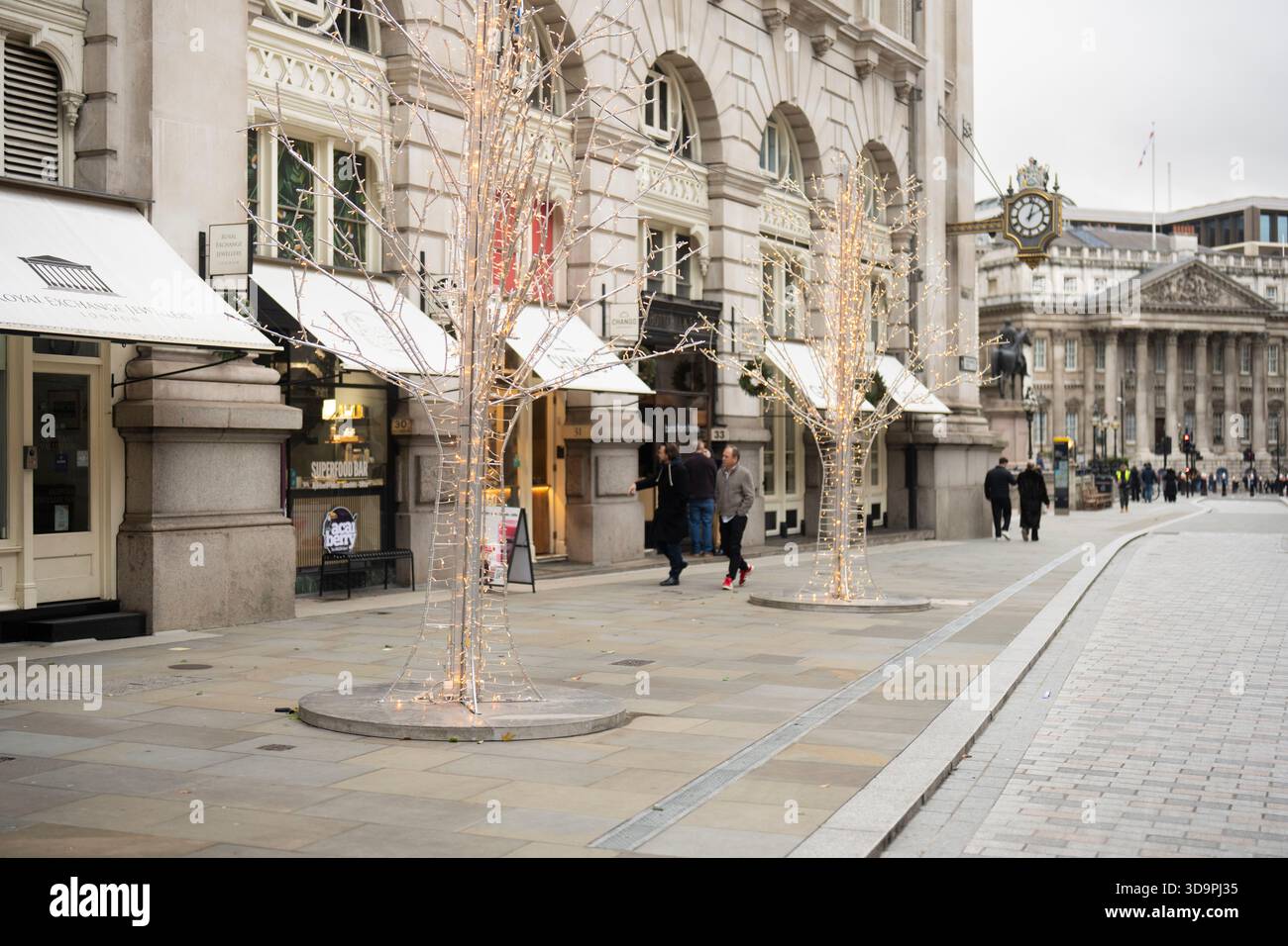 Le persone camminano davanti agli alberi illuminati all'esterno del Royal Exchange, Londra, durante le festività. Foto Stock