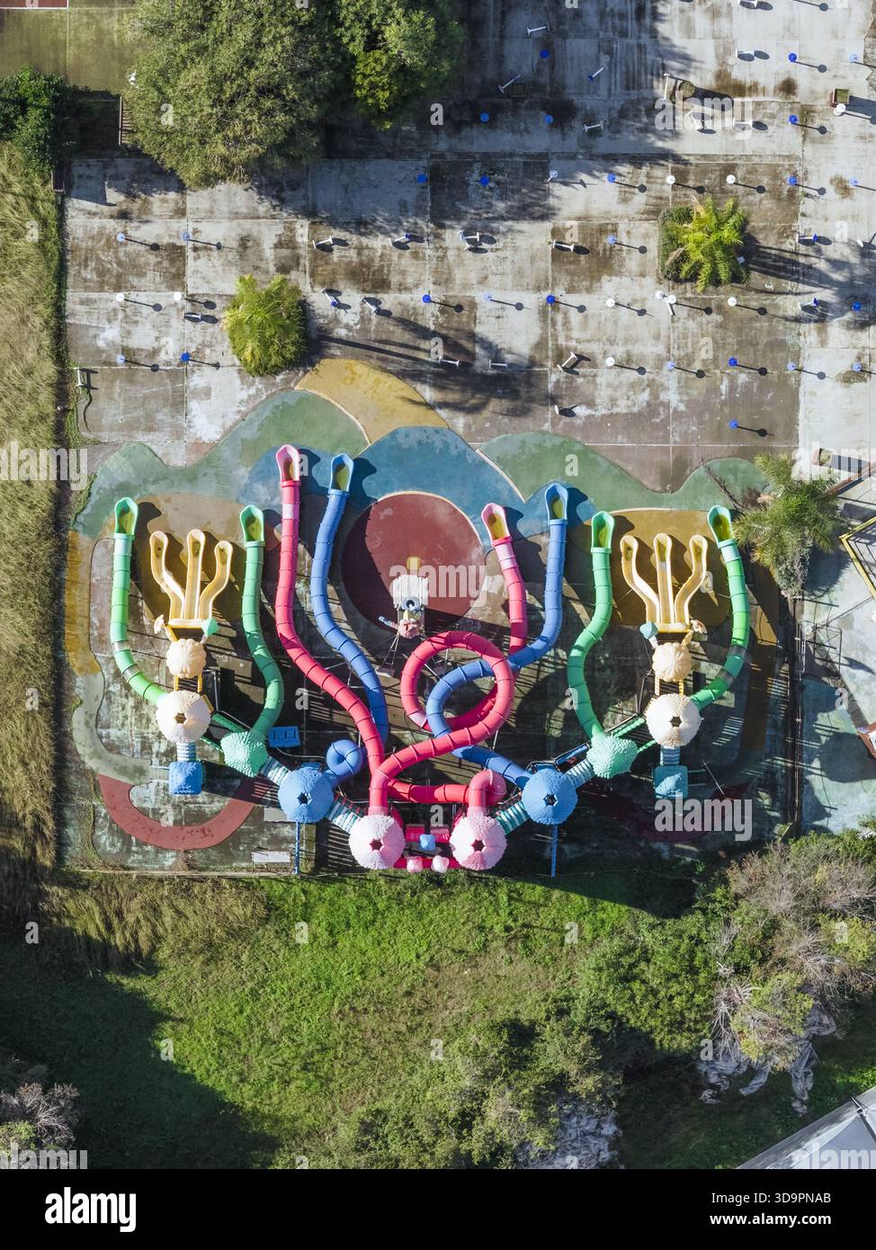 Vista aerea di un vivace parco giochi con colorate strutture simili a polpi che si stagliano contro il cemento intempestivo, circondato da erba verde, Batt Foto Stock