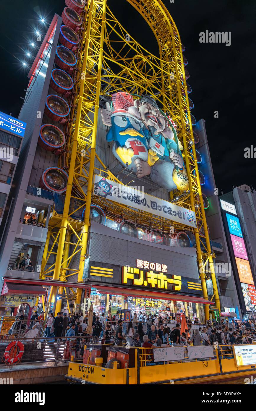 La gigantesca ruota panoramica gialla di Don Quijote e l'enorme cartellone dei cartoni animati illuminano l'affollata passeggiata del vibrante quartiere Dotonbori di Osaka. Foto Stock